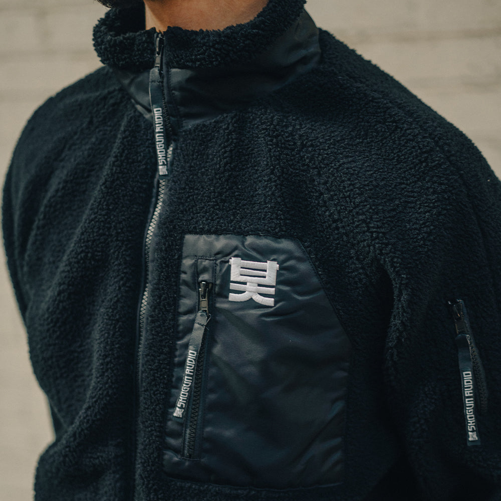 Black fleece jacket with a brand logo on a neutral background