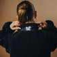 Person wearing a black jacket with a brand logo on a beige background